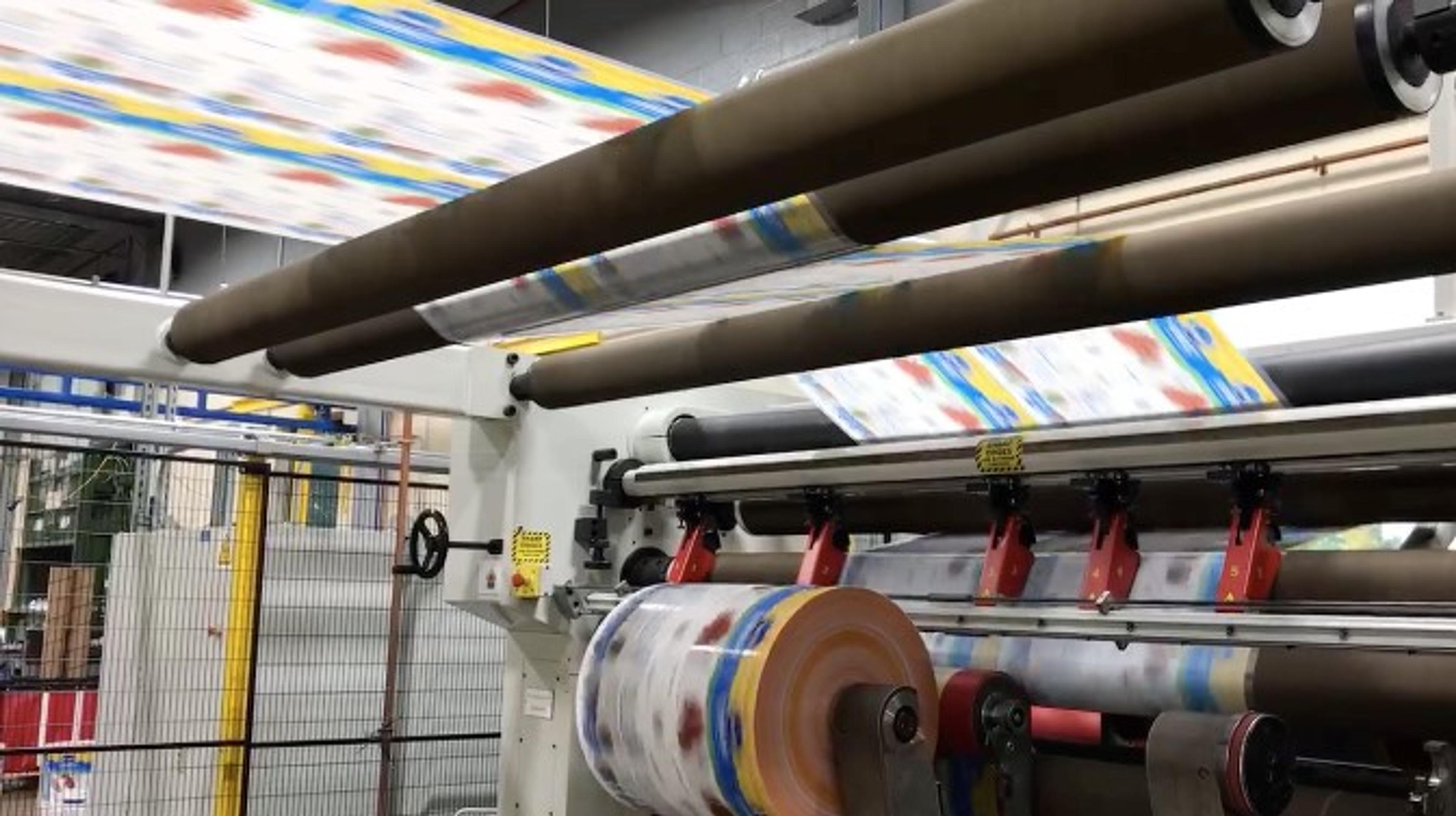 Printed flexible packaging film web running over rollers and rewinding onto a roll in a converting line.