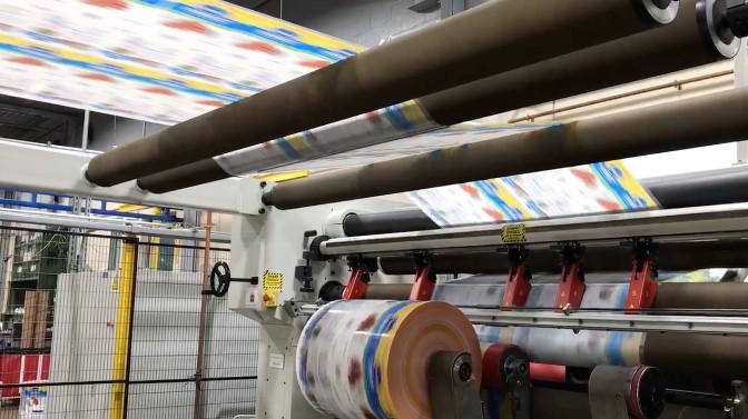 Flexible film printing and rewinding Printed flexible packaging film web running over rollers and rewinding onto a roll in a converting line.