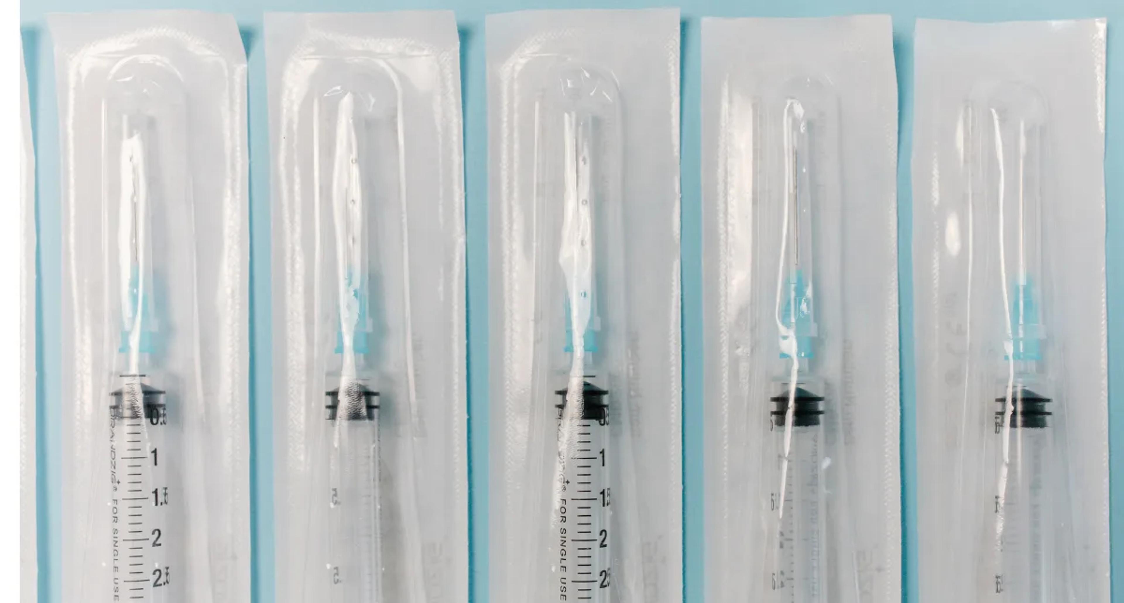 Five sterile syringes individually sealed in clear medical blister pouches on a light blue background