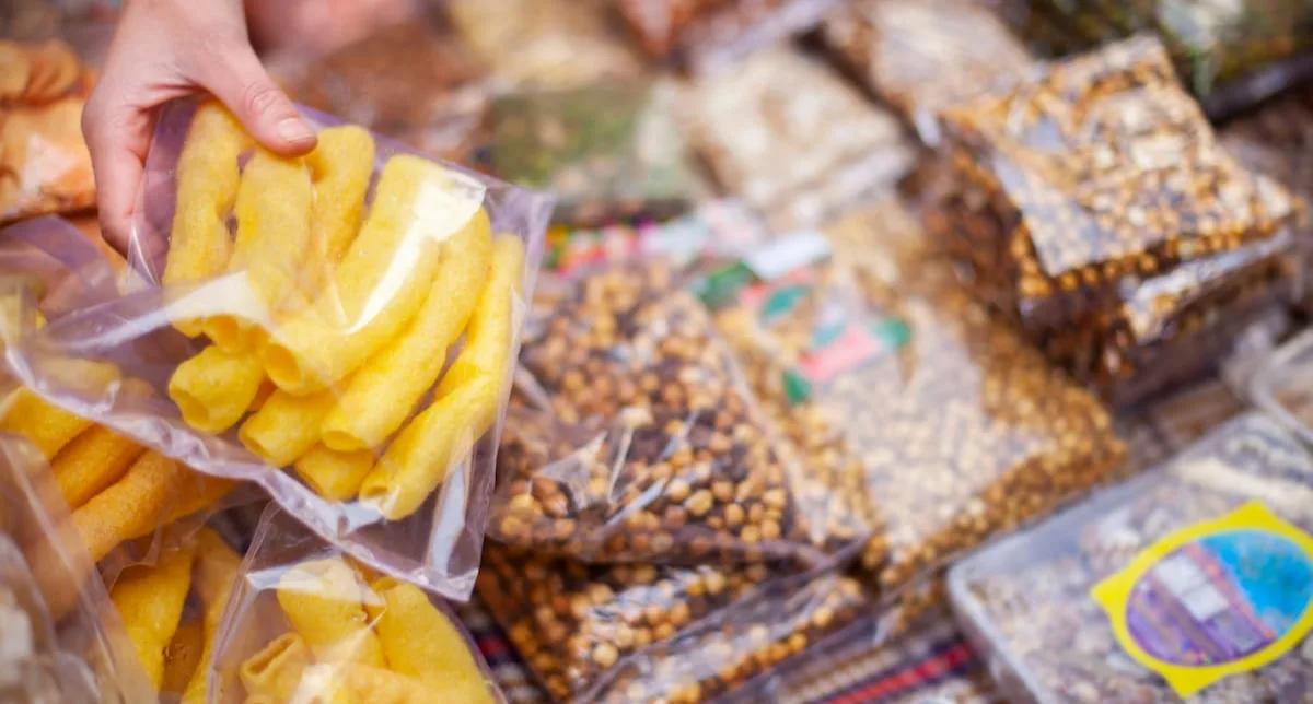 Hand placing snacks in clear CPP bag Hand placing puffed corn snacks into a clear resealable cast PP (CPP) bag among other clear-sealed snack packs