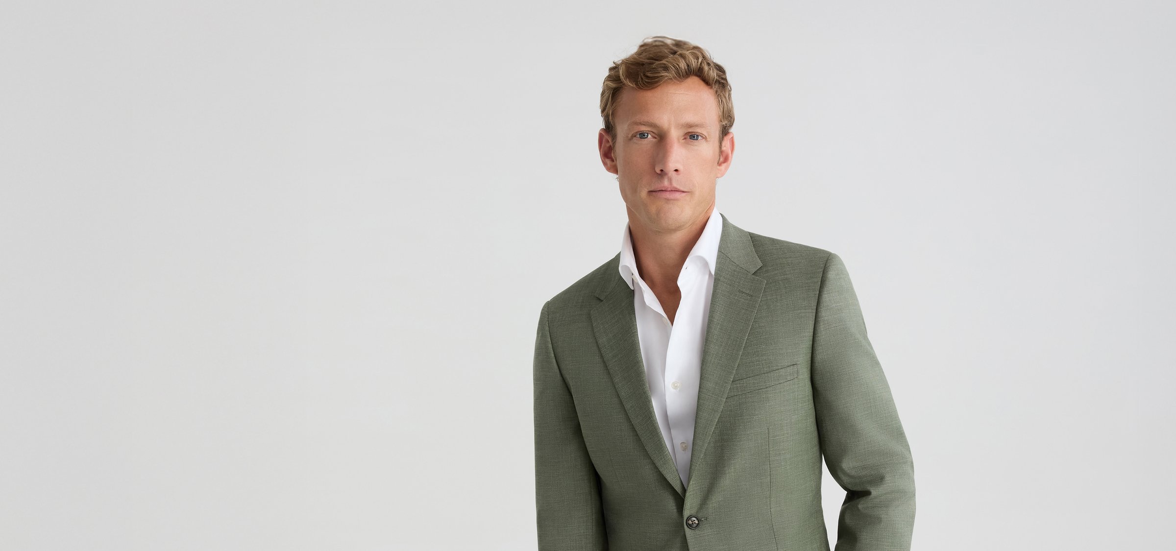 Smiling man wearing a linen-look light olive green suit, the vibe is spring and bright
