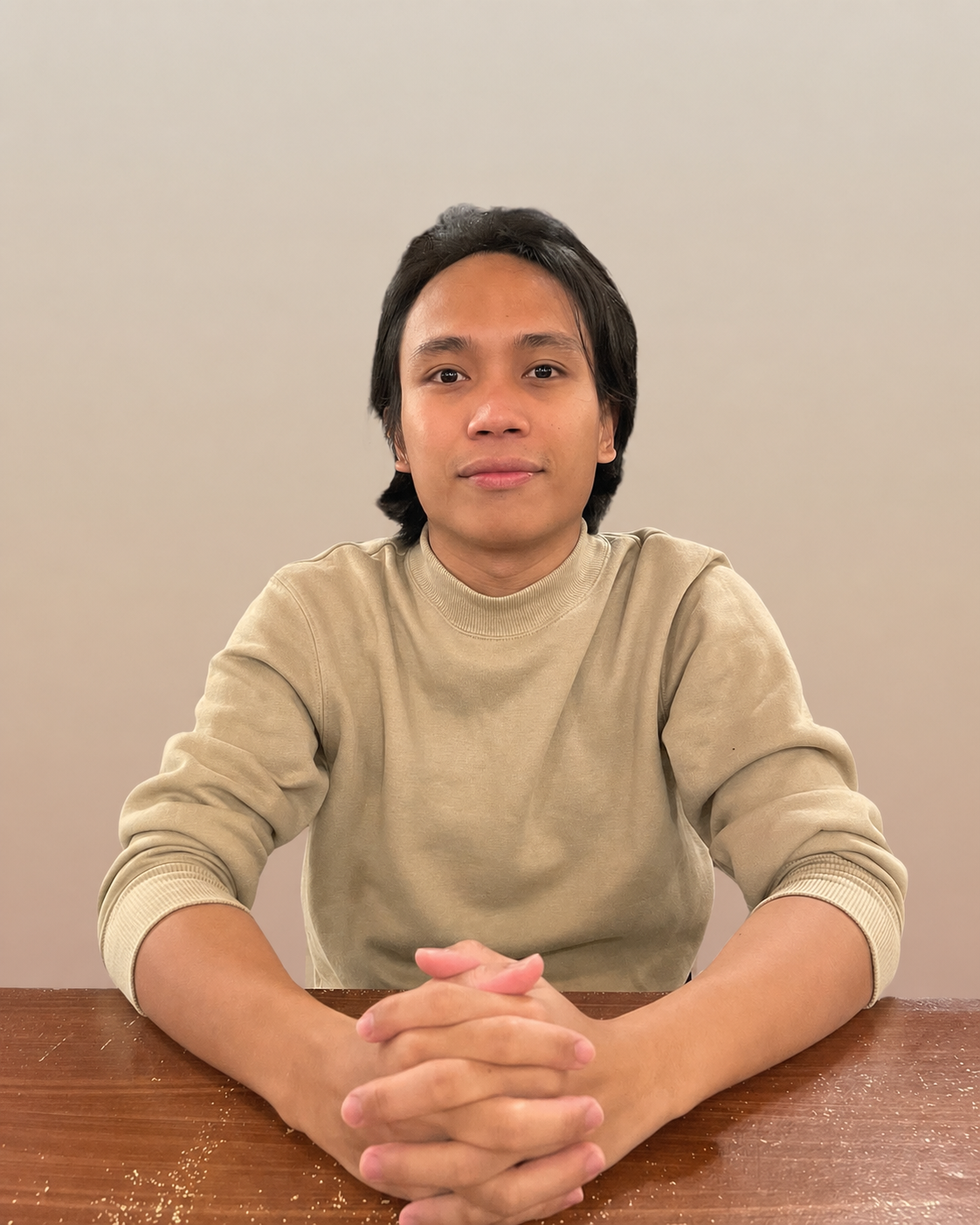Portrait of Elloani Pitogo, wearing beige sweatshirt, seated at a table with hands clasped
