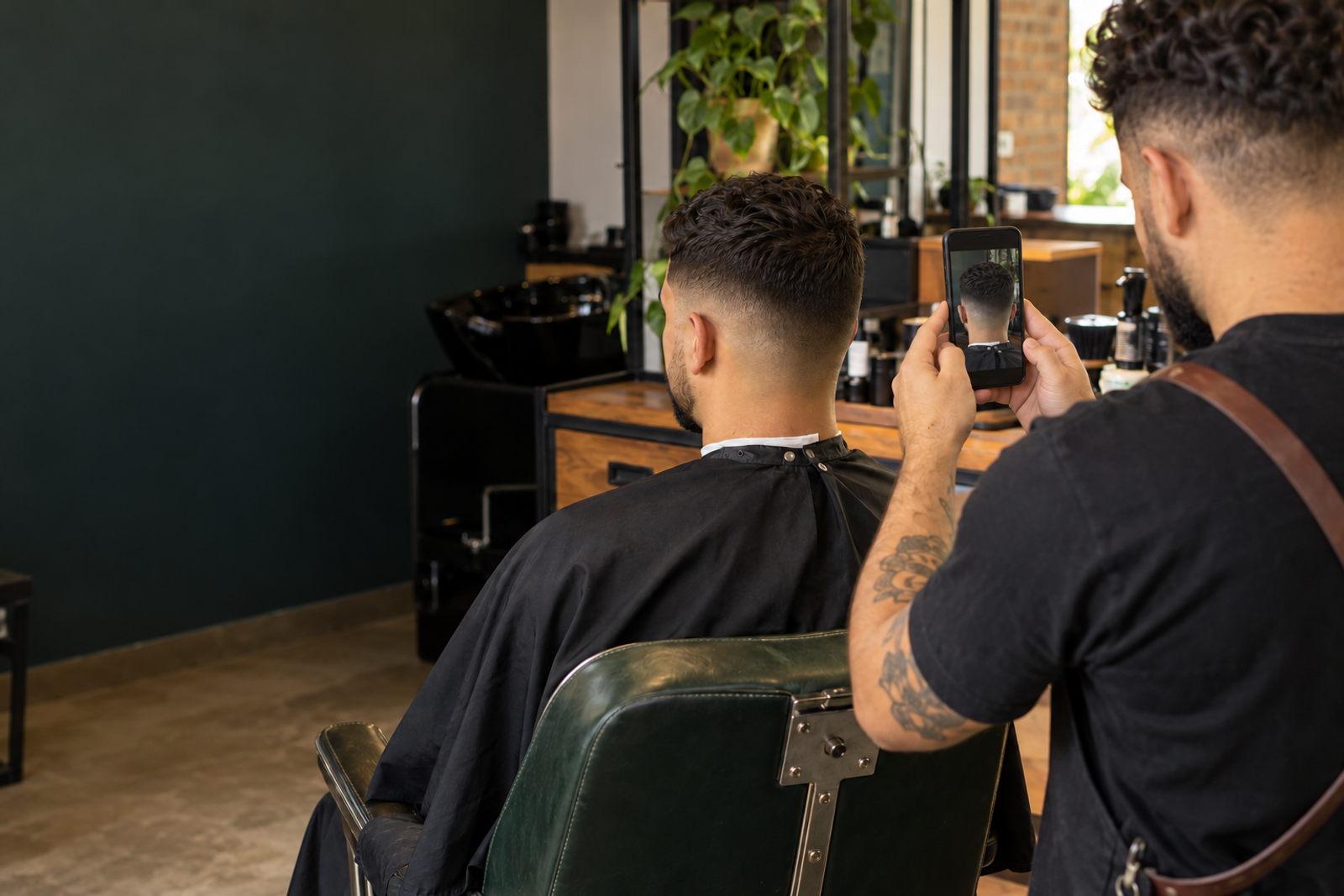 Barbeiro registra o corte de um cliente de costas em uma barbearia iluminada.