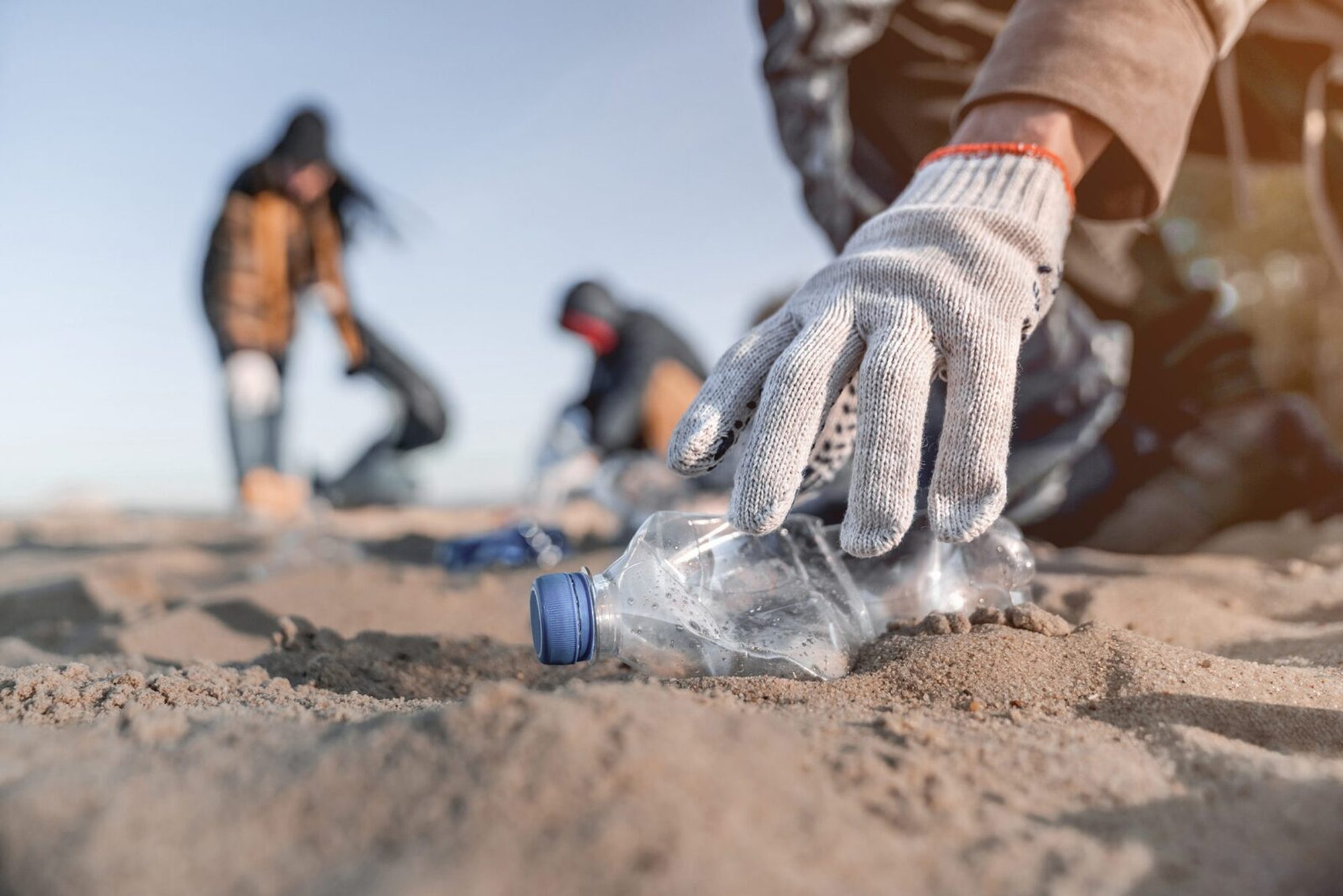 Gloved hand collecting a plastic bottle from sand