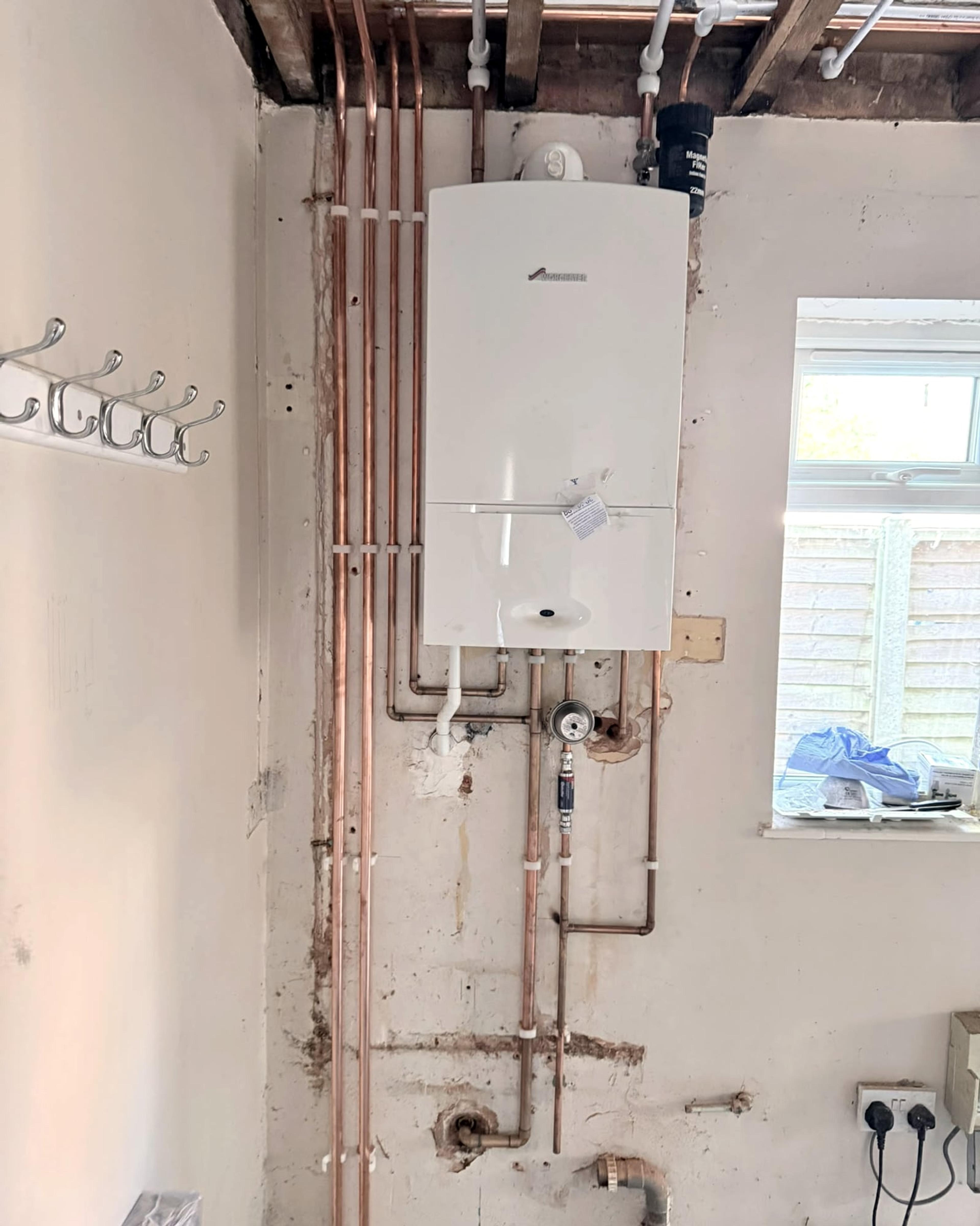 The boiler from the front, with copper pipes running up the wall into the open ceiling