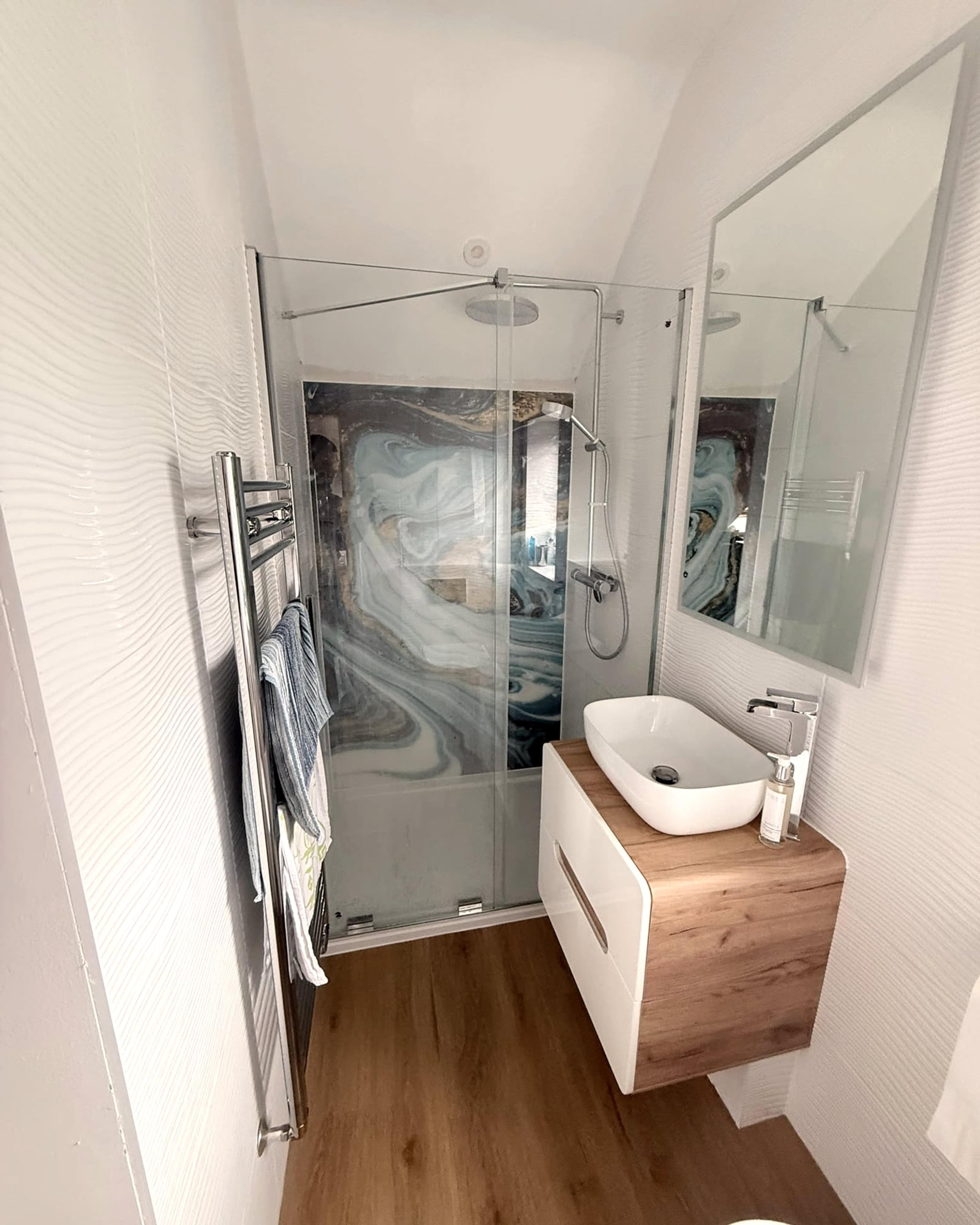 A small en suite with a glass shower enclosure, marble-effect panel, oak vanity unit and vessel basin