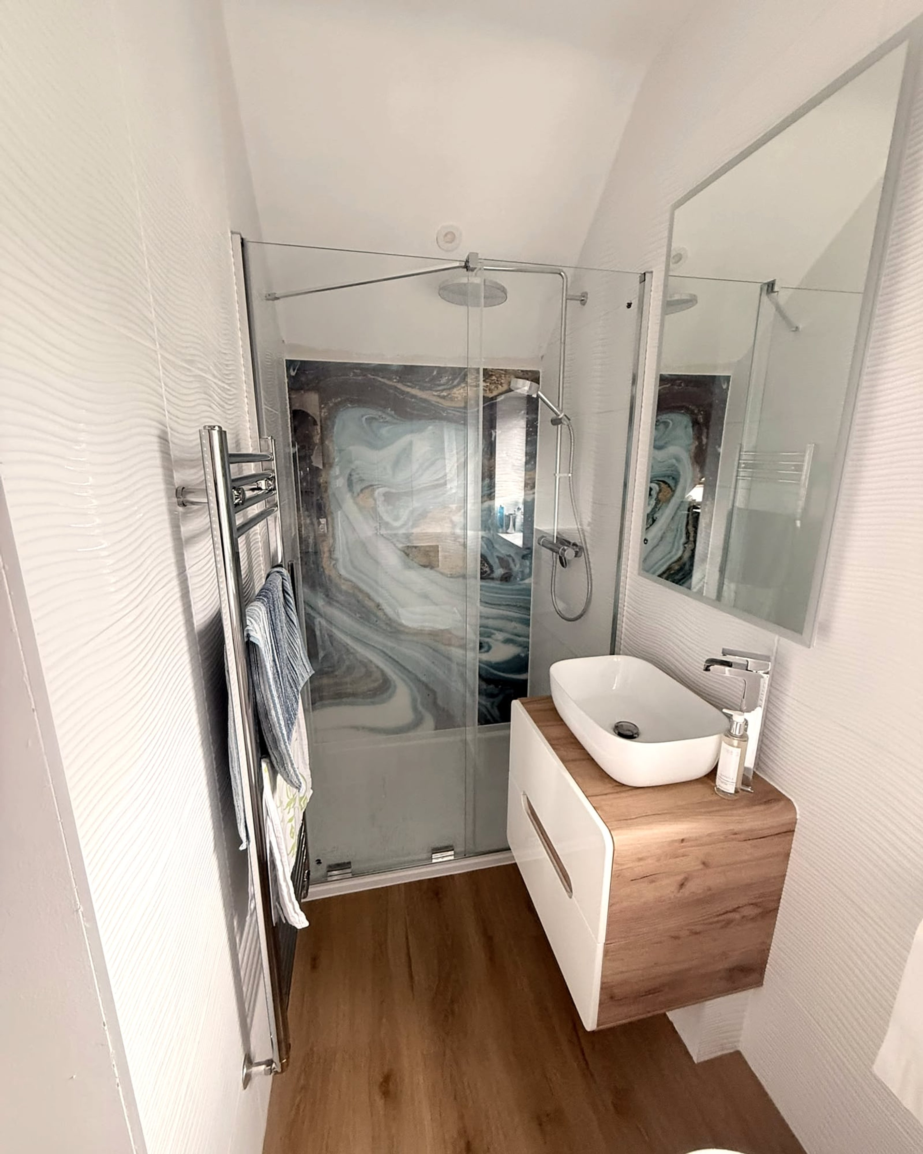 A small en suite with a glass shower enclosure, marble-effect panel, oak vanity unit and vessel basin