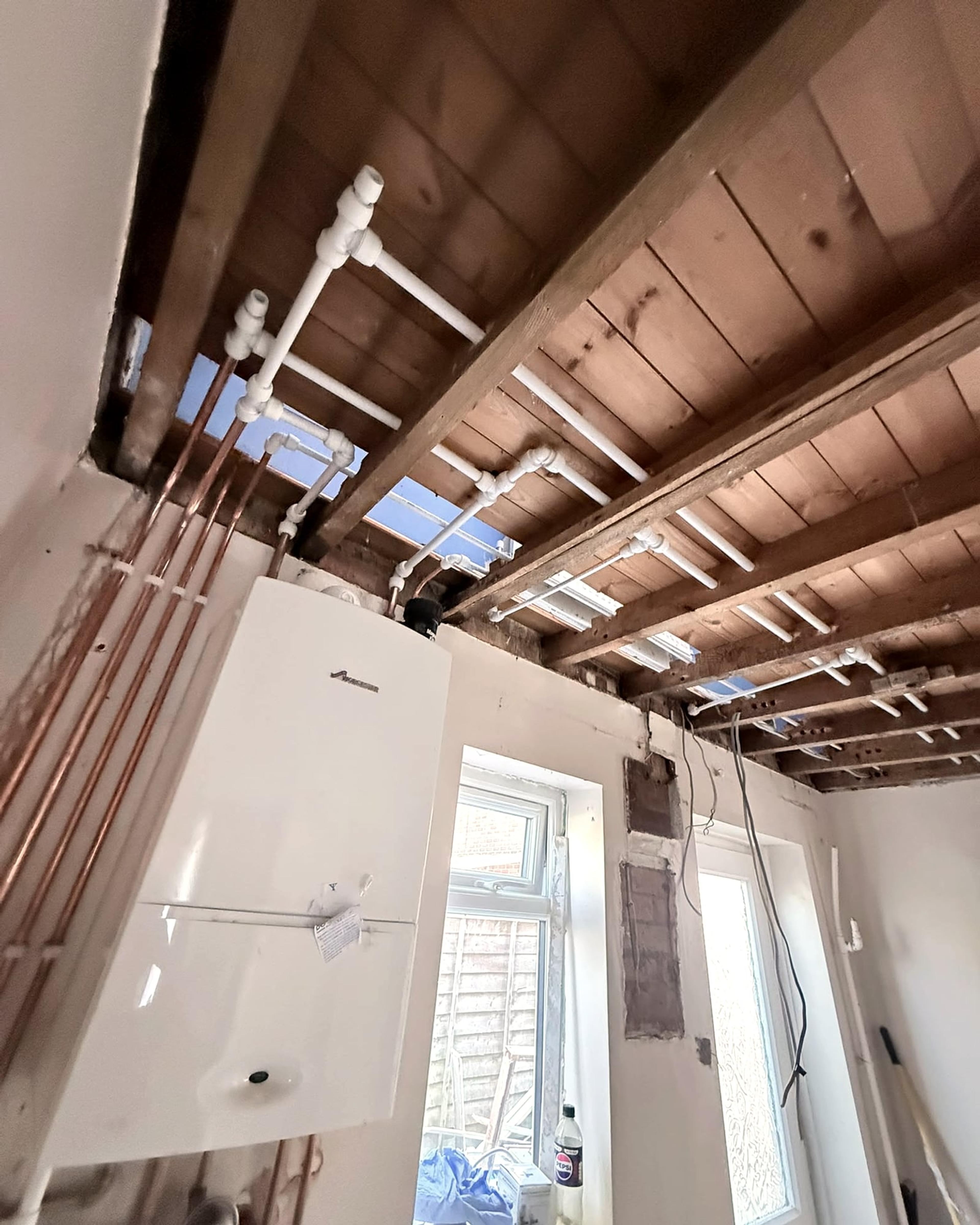 Copper and plastic pipe runs between exposed ceiling joists above a newly fitted boiler