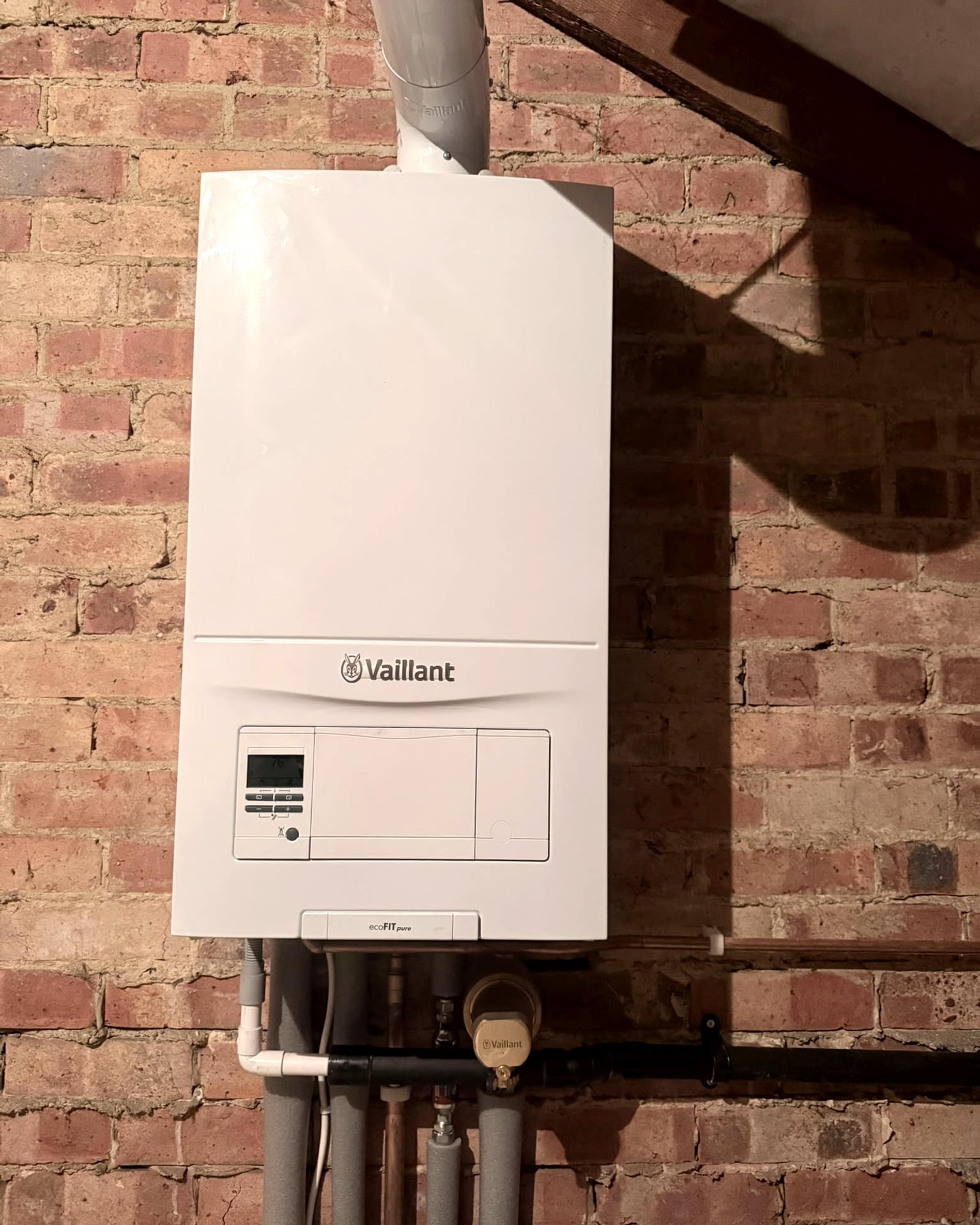 The boiler close up on the brick wall, with its pipework and controls below