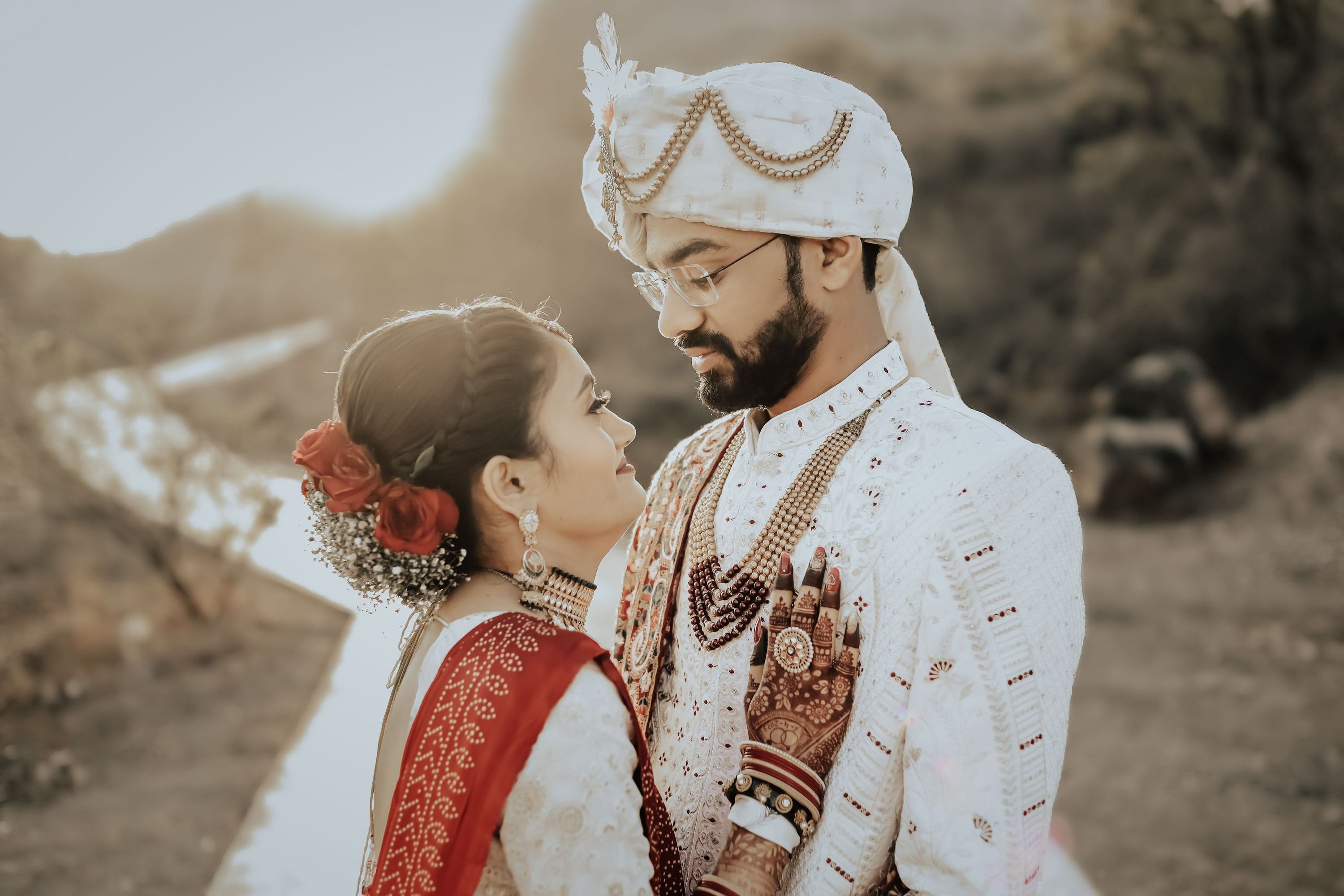 Bride and groom in white sherwani and red lehenga sharing a quiet moment at sunset