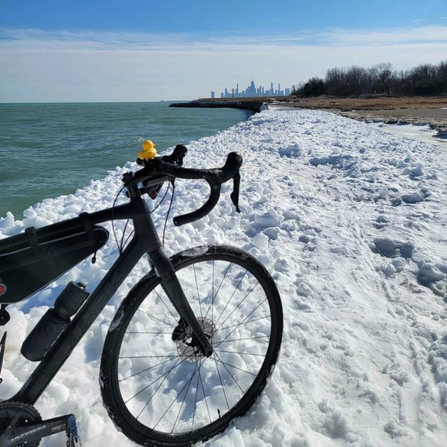 Photo of a black bike with drop bars on snow at the beach. The Chicago skyline is in the background.