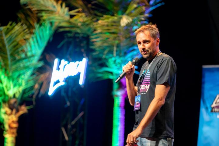 A speaker with a microphone beside the neon Latency sign at Latency 2021