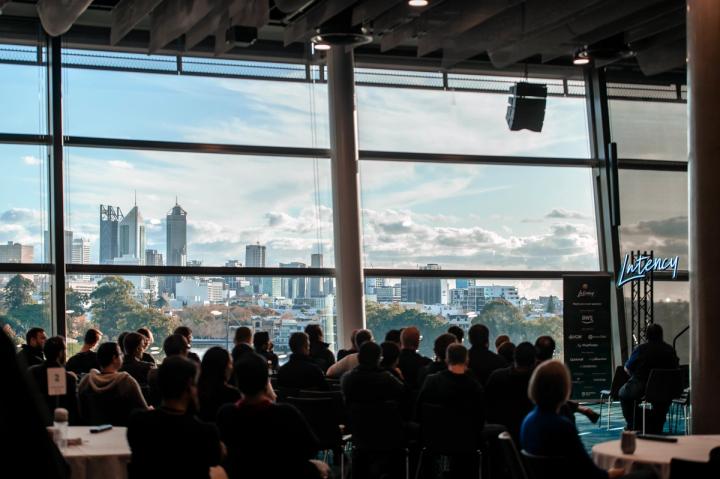 An audience in front of windows looking out over the Perth skyline at Latency 2023