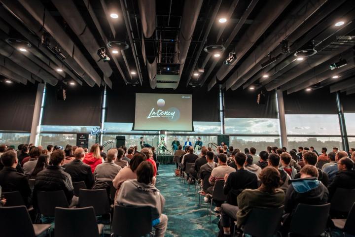 A full hall facing the stage and the Latency screen at Latency 2023