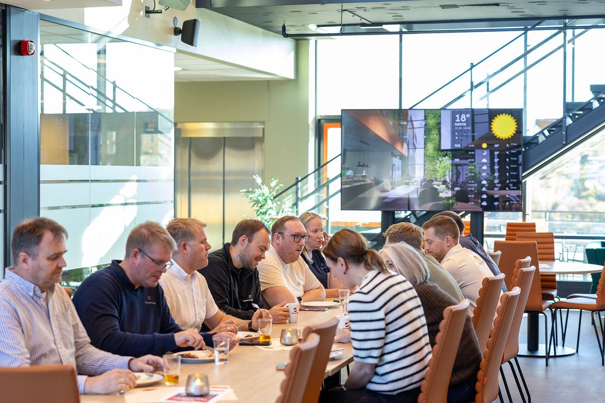 Kolleger spiser lunsj sammen ved et langbord i kantina.