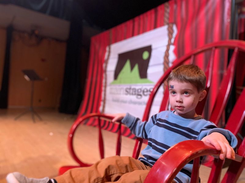 4 year old boy sitting on a red rocking chair in front of a mainstages backdrop