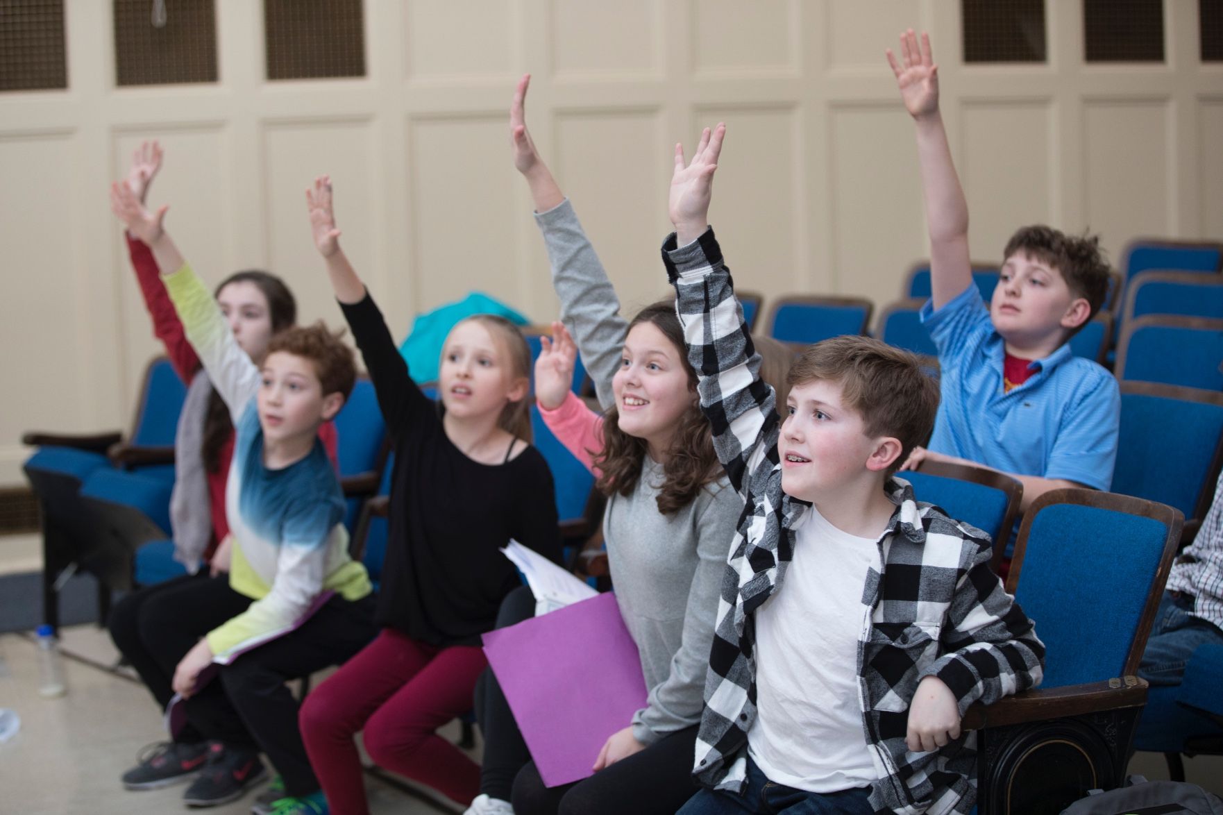children with hands raised eager to answer a question