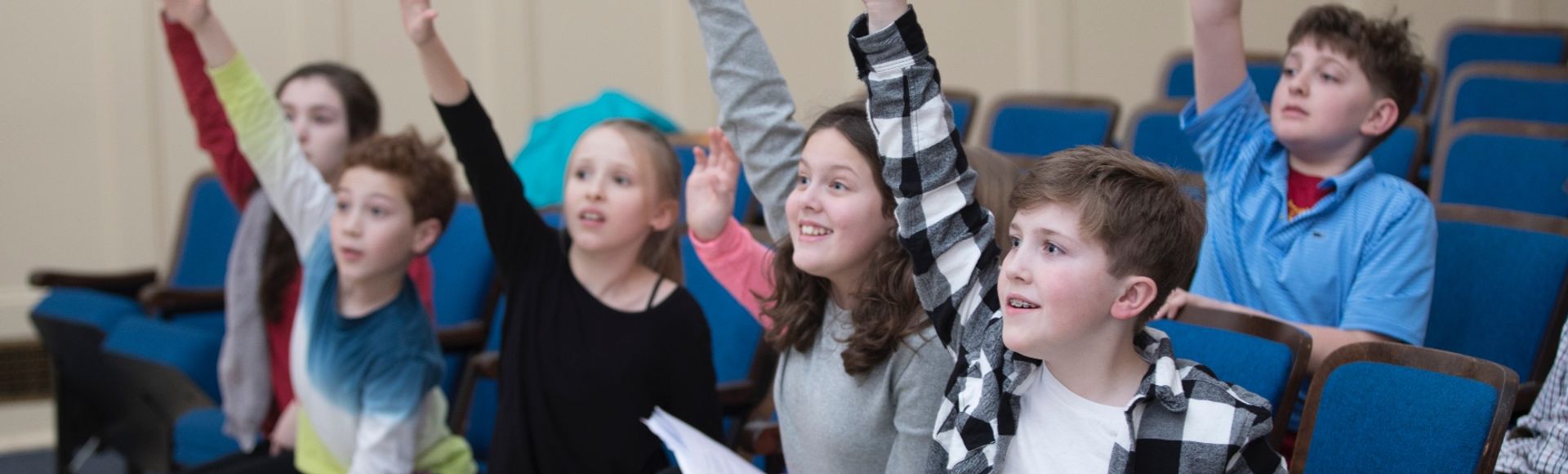 children with hands raised eager to answer a question