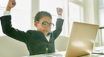child raising their arms in triumph sitting in front of a computer screen