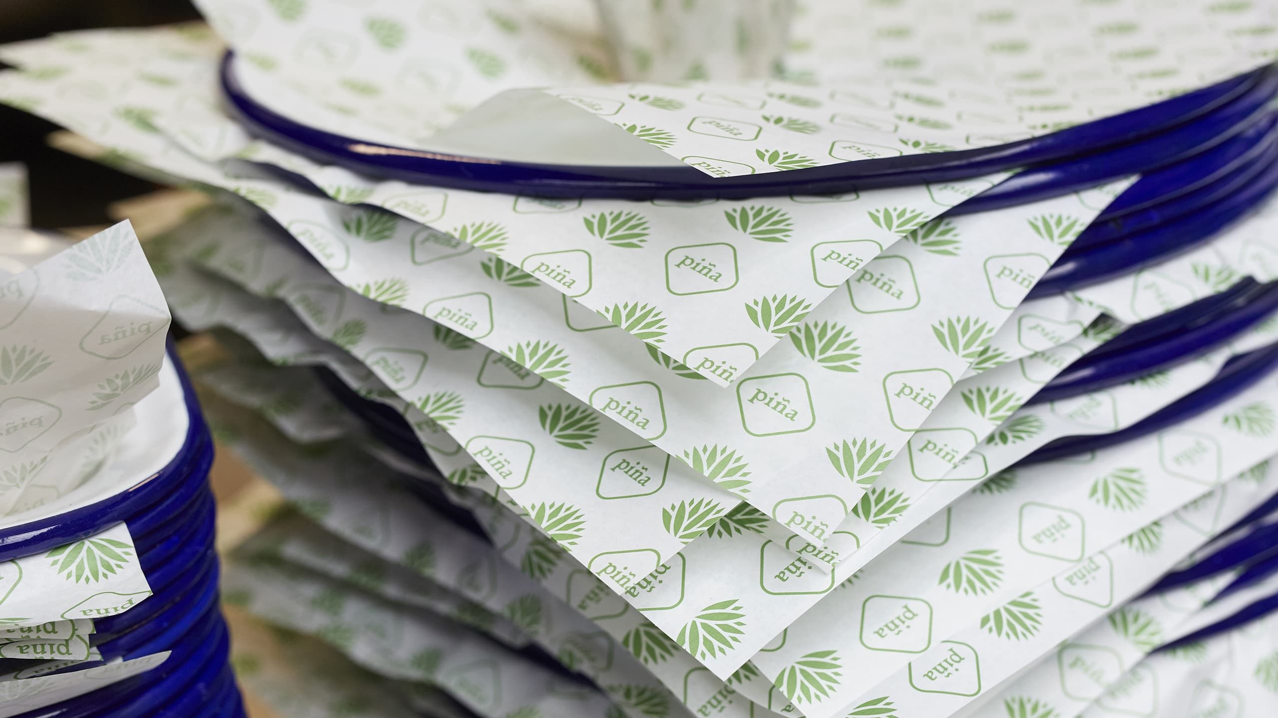 A stack of plates covered with piña branded greaseproof paper ready for service.