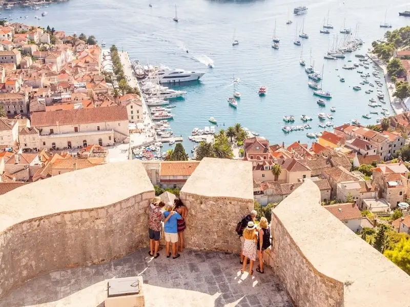 View of Hvar Town in Croatia from the Spanish Fortress with travellers overlooking the harbour, sailboats and yachts, a popular stop for island hopping and sailing holidays in the Adriatic.
