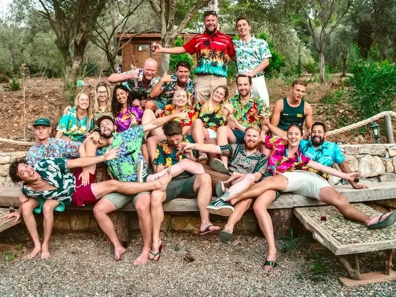 Group of people laughing and enjoying life, dressed in colourful island clothing, while on a sailing week stag do and hen do with MedSailors. They are partying on an island while exploring and sailing together on a group bachelor and bachelorette trip.