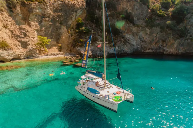 A MedSailors catamaran anchored in a bright blue bay in Turkey with people swimming.