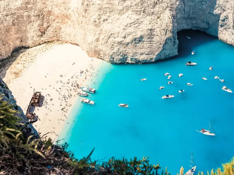 Aerial view of Navagio Beach (Shipwreck Beach) in Zakynthos, Greece, with bright turquoise Ionian water, white limestone cliffs, a sandy cove and boats anchored offshore near the famous shipwreck. Image used in a MedSailors Odyssey locations in Greece guide to highlight Zakynthos as a dramatic Ionian island stop, combining epic coastal scenery, sea caves and sailing routes that fit the adventurous, seafaring spirit of Homer’s The Odyssey.
