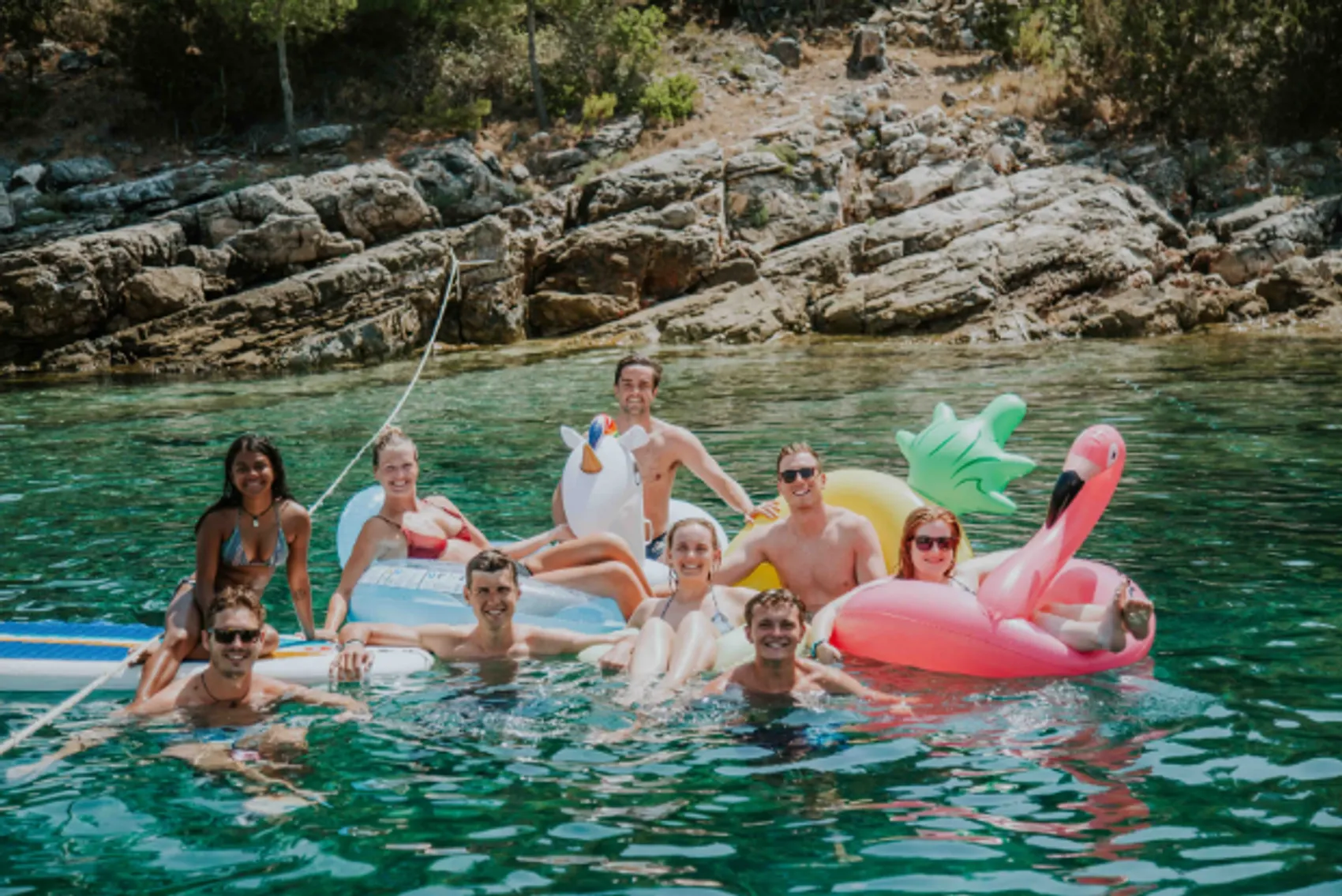 A group of young travellers in floaties in a beautiful bay in the Mediterranean. 