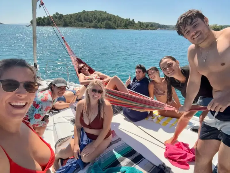 Group of young travellers relaxing on a yacht during a swim stop on a Greek island hopping trip from Athens. Friends enjoying sunshine, turquoise water, and social sailing vibes on an affordable summer holiday in Greece.