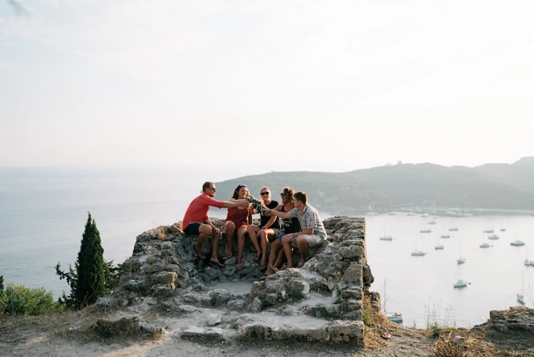 Group of people sitting atop ruins on the Parga fortress in Greece at sunset with beers.