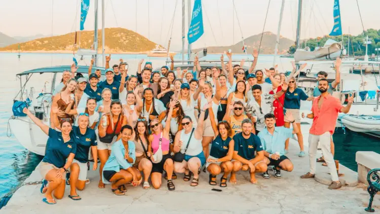MedSailors travellers enjoying a group gathering on a rooftop terrace in Croatia, alongside a view of Hydra island in Greece, showcasing social sailing holidays, new friendships and Mediterranean island adventures.