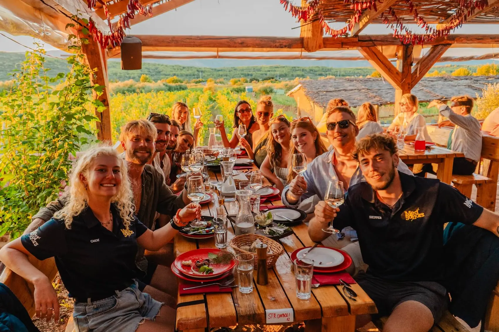 Group of young travellers at a table sharing traditional Croatian food and wine on an organic farm in Stari Grad.