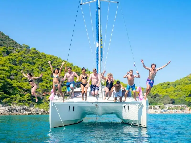 Youth travellers and Aussie or Kiwi exchage students on a sail week in Croatia with MedSailors jumping off of a catamaran in a blue bay.
