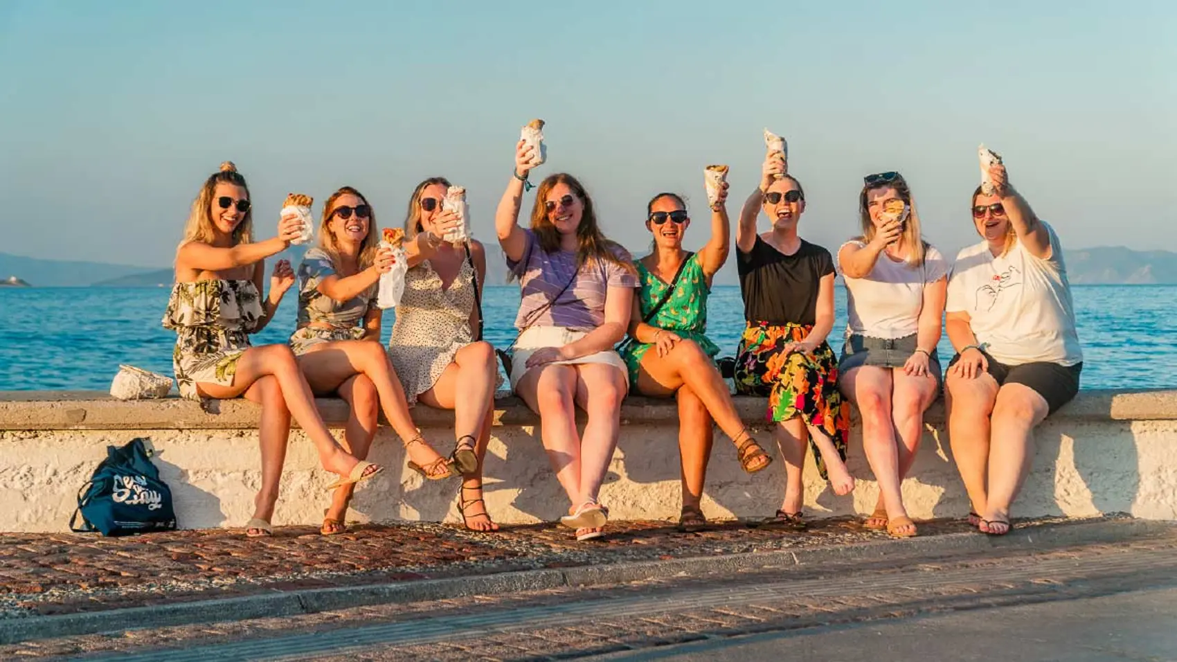 Group of friends eat gyros on the waterfront in Hydra