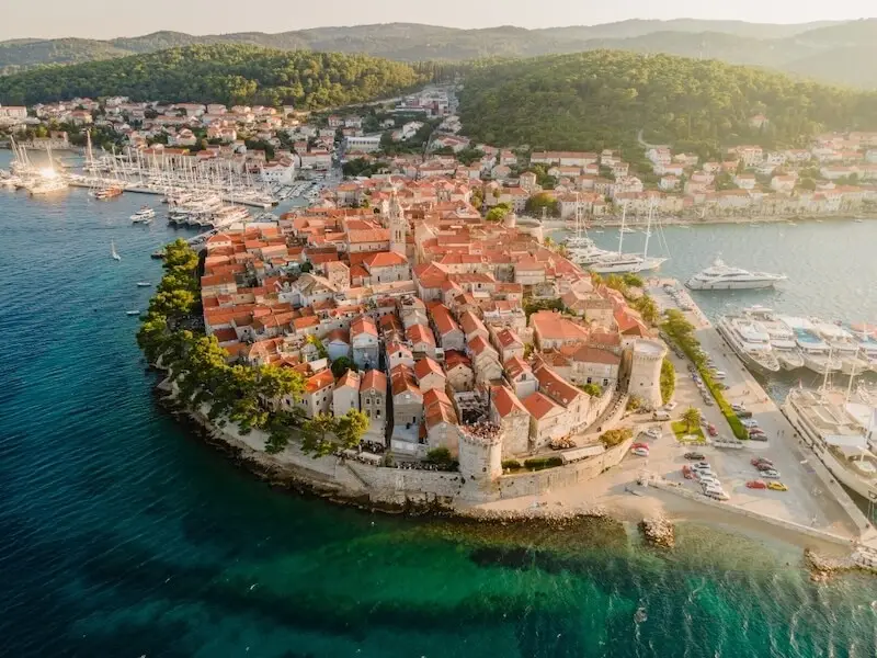 Aerial view of Korčula Old Town in Croatia with its medieval walls, red rooftops, marina and clear Adriatic water, a popular stop on Croatia island hopping and sailing holidays.