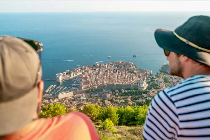 Two travellers look out over the Croatian city of Dubrovnik from a mountain viewpoint while on a Croatia island hopping trip.