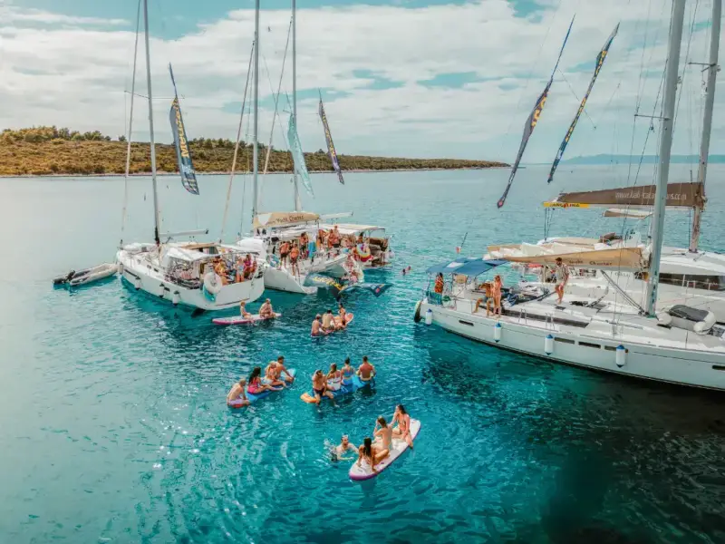 MedSailors yachts rafted together in clear turquoise water in Croatia, with travellers swimming, paddleboarding, and relaxing during a summer sailing holiday. Image for a budget guide about combining Ultra Europe in Split with a Croatia island hopping trip, yacht accommodation, swim stops, and a social sailing route with MedSailors.