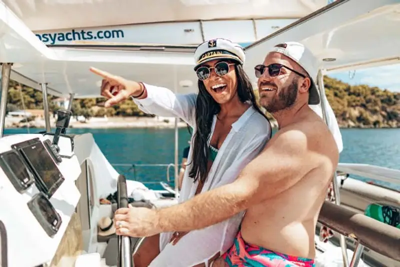 A male and female at the helm of a catamaran yacht while on a Mediterranean island hopping trip with MedSailors.