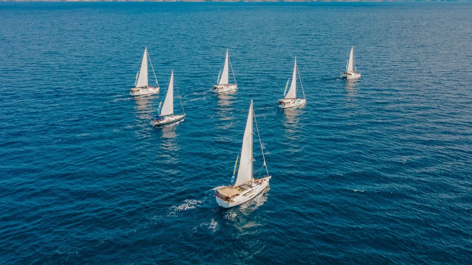 Aerial view of five MedSailors yachts sailing across deep blue Mediterranean waters on a sustainable sailing holiday in Greece or Croatia