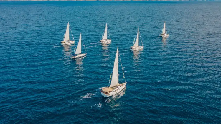 Aerial view of five MedSailors yachts sailing across deep blue Mediterranean waters on a sustainable sailing holiday in Greece or Croatia