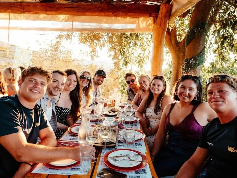 Group of travellers enjoying a shared dinner with wine at a long outdoor table in Croatia during a warm summer evening.