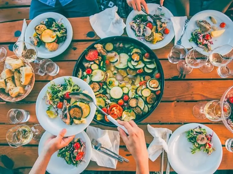 Overhead view of a shared Mediterranean meal with fresh vegetables, bread, and wine on a wooden table in Croatia.