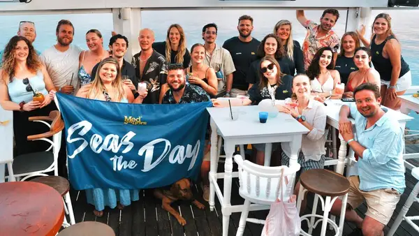 MedSailors welcome party at a cocktail bar at sunset, with a group of young travellers meeting and celebrating the start of the trip. Located at Ermioni port in the Saronic Gulf near the Peloponnese, an overlooked gem of a Greek sailing destination.