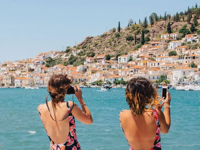 Two travellers capturing the stunning seaside town of Poros, one of the best Greek islands near Athens, known for its whitewashed houses, crystal-clear waters, and rich history.