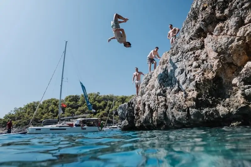 Travellers cliff jumping into clear blue water during a MedSailors Greece island hopping sailing holiday, showing the adventure and social atmosphere of the trip.