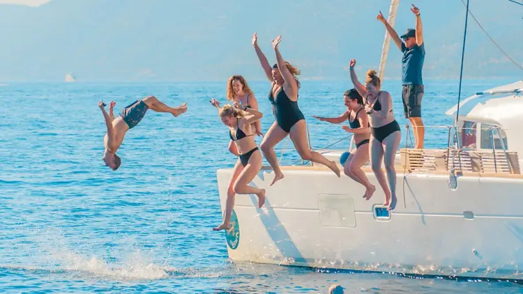 MedSailors travellers jumping from a catamaran into the blue Mediterranean Sea during a group sailing holiday, enjoying swimming, adventure and unforgettable moments with friends.