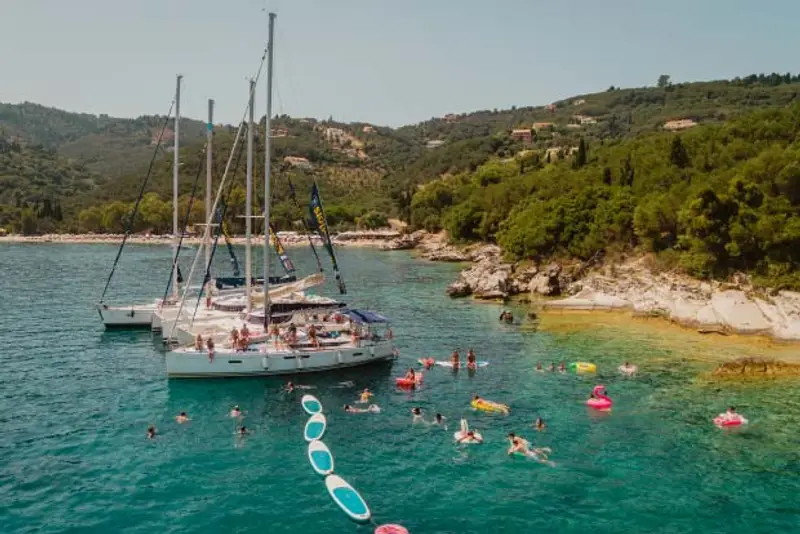 A raft of yachts on a sail week trip with MedSailors as adventure travellers of 20s and 30s swim in a turquoise bay.