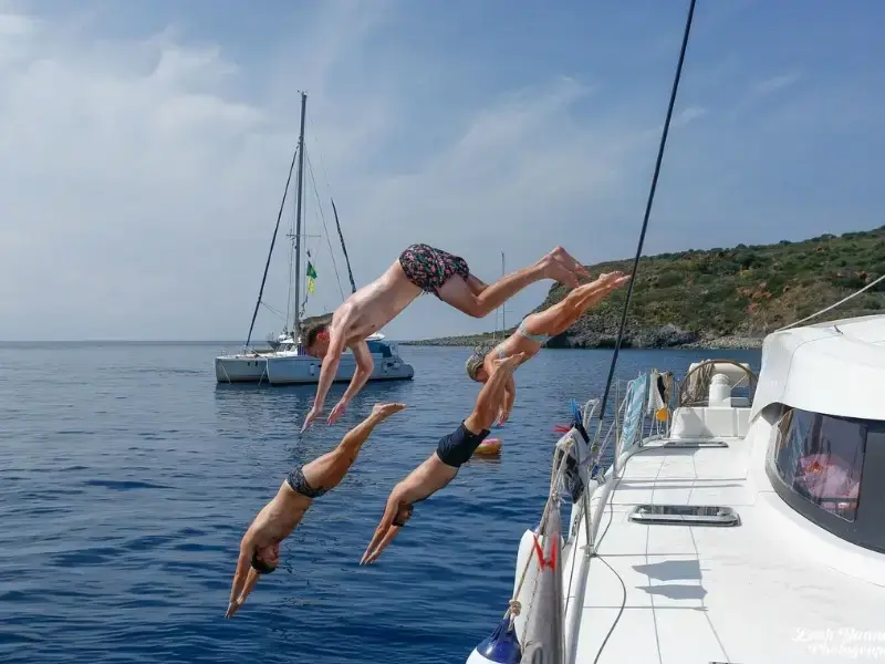 Young travellers diving off a yacht into calm blue water during a sailing trip in Croatia, capturing the fun and social side of island-hopping in Europe. This image reflects typical moments on group sailing holidays where swim stops, boat days, and shared experiences are central to the journey, highlighting why travel insurance that covers water activities can be important for active travellers.