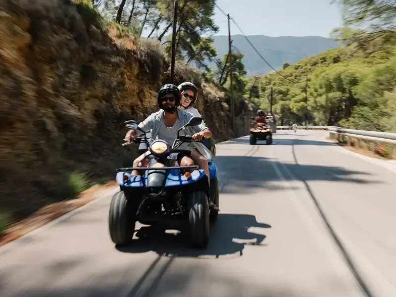 Young travellers riding a quad bike along a scenic coastal road in Europe, capturing the freedom and adventure of exploring destinations like Croatia and Greece. This image reflects popular activities such as scooter and quad bike hire during backpacking trips, where travel insurance that covers road activities and rentals can be important. Ideal for illustrating Europe travel, island exploration, and adventure activities for young travellers.